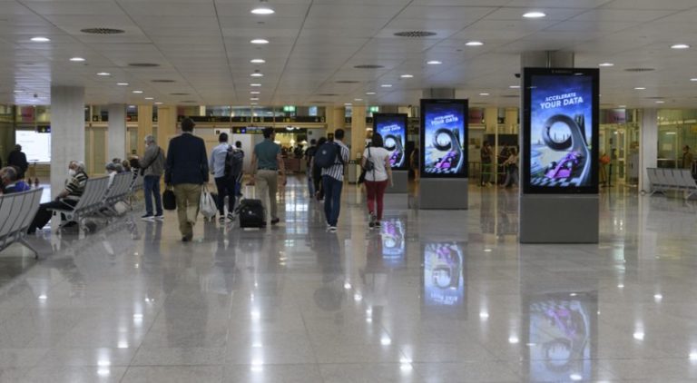 In the center of the image at Barcelona Airport, many people are visible, and on the right, three digital City Light Posters are lined up in a row. The digital screens display product advertising for Ataccama Software.