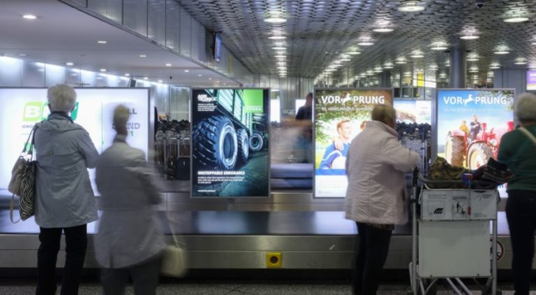 At the baggage claim at Hannover Airport, four lightboxes are visible. People are standing in front of them. They display an advertisement for Nokian Tyres.