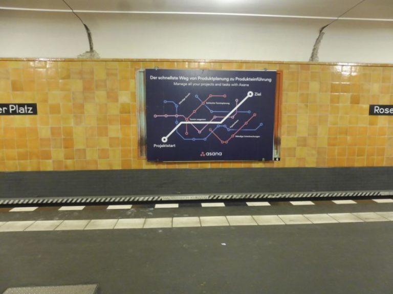 At the Berlin subway station Rosenthaler Platz, there is a large advertising space behind the tracks. The poster advertisement features a time management platform by Asana.
