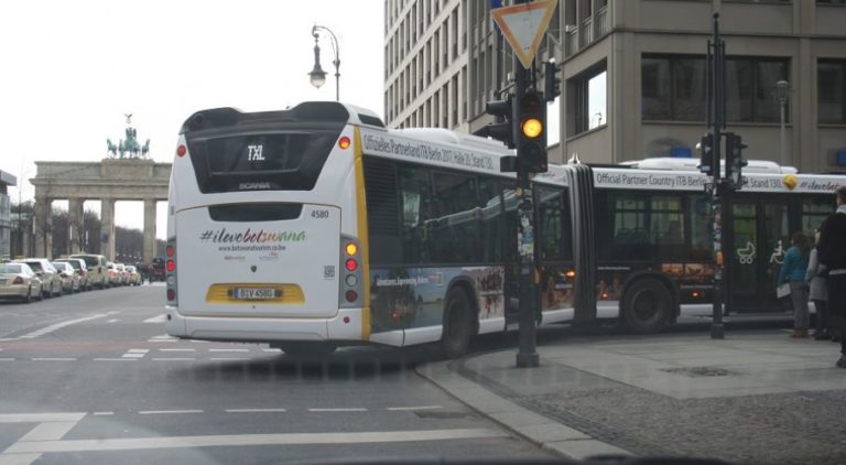 A bus, turning right on a street in front of the Brandenburg Gate, displays a Full Cover advertising motif of Botswana.