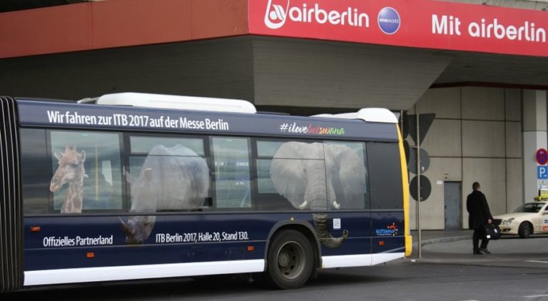 On the side of the rear part of a bus, a Full Cover advertising motif of Botswana is recognizable. In the background, a pedestrian and a building with the inscription "AIRberlin" are visible.