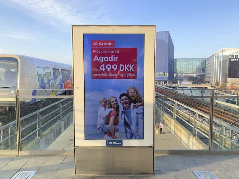 In Copenhagen, a Digital City Light poster with AirArabia advertising is visible in the center of the foreground. On the lower left side in the background, a train is visible, while the tracks run to the right.