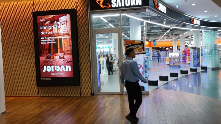 In a Frankfurt shopping center, on the left, a digital City Light poster with advertising for Jordan is visible. In the middle of the image, a person is passing by, and you can see the Saturn store extending to the right.
