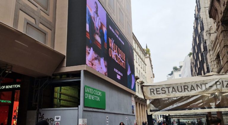 A large digital screen displays Snipes advertising. The photo was taken in the middle of a shopping street between two residential buildings. Snipes advertising is visible on the left side.