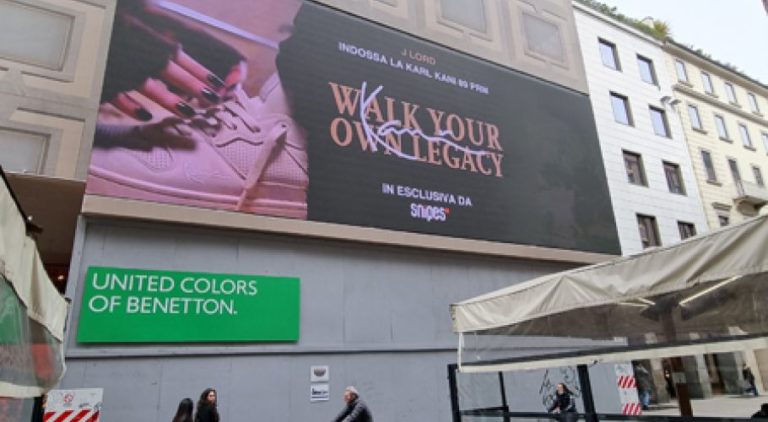A large digital screen on a residential building in Milan, which slightly stands out from the two surrounding buildings, displays Snipes advertising. Pedestrians walk beneath the screen.