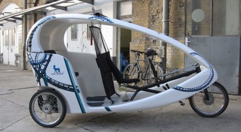 In front of a building, there is a white three-wheeled taxi with a Full Cover advertising motif from Novo Nordisk.