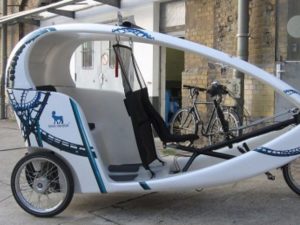 In front of a building, there is a white three-wheeled taxi with a Full Cover advertising motif from Novo Nordisk.