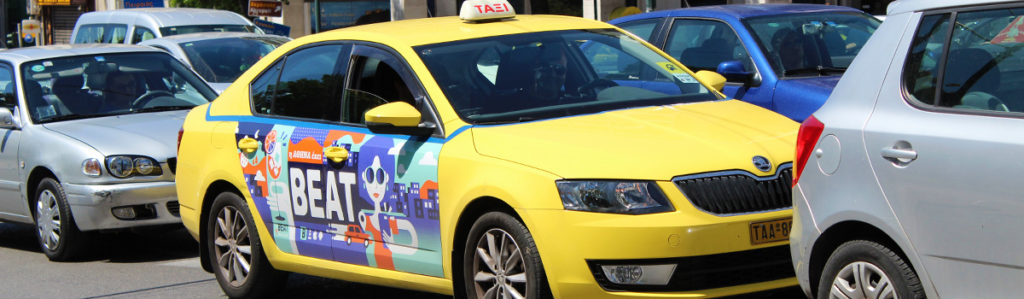 A yellow taxi with a colorful taxi-ad on the right door