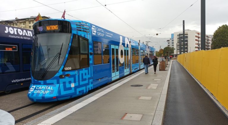 At a stop in Geneva, a tram with a Full Cover design promoting the Capital Group is standing. Two pedestrians are walking by on the right.