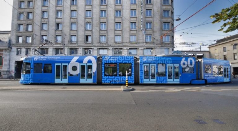 In the city center of Geneva, a tram with a blue Full Cover design advertising the Capital Group is running.