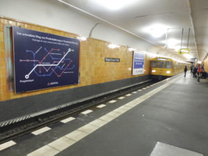 A subway is arriving at the station. Many people are trying to board, and on the left side, there is a large analog billboard advertisement.