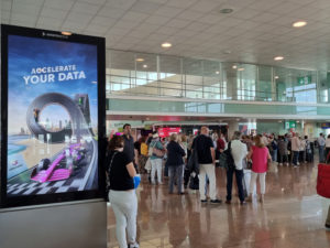 A person leans against a digital billboard at a crowded airport.