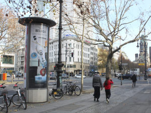 An advertising column featuring a Beluga advertisement stands in the middle of Berlin at a busy intersection.