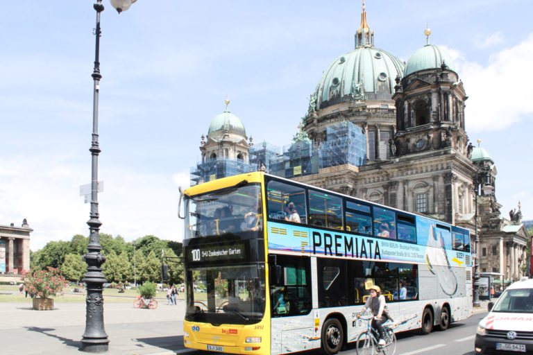 A bus with a full-cover travel advertising motif is parked in front of the Berlin Cathedral on the street.