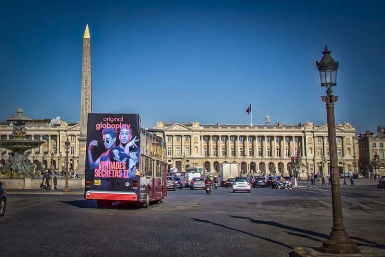 In Paris, in front of the Place de la Concorde, a sightseeing bus with Super Rear advertising is visible. The design belongs to Globoplay Originals.