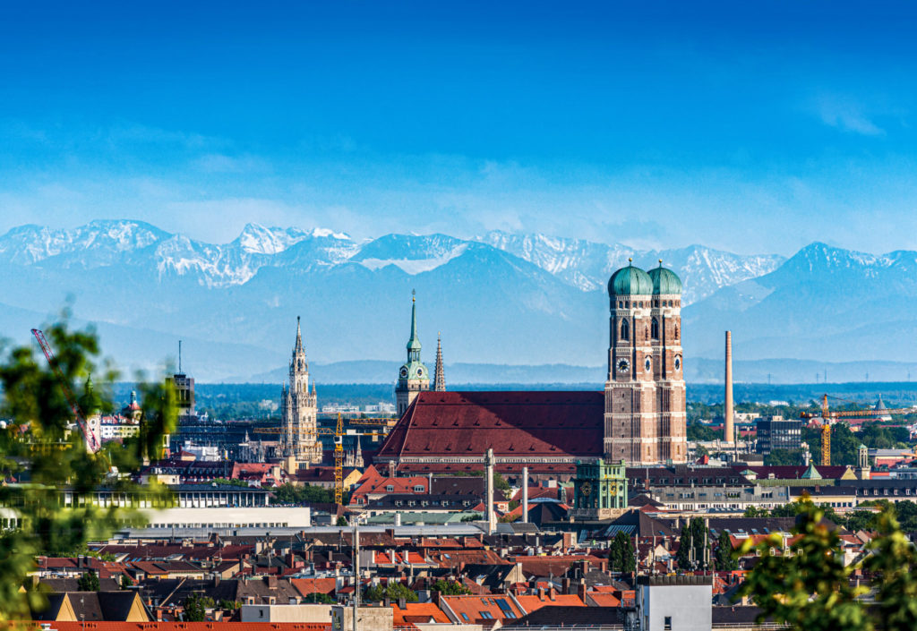 View of Munich from above. In the center, you can see the landmark, the Frauenkirche, with the Alps in the background.