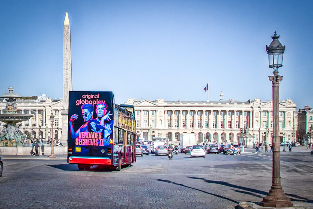 A sightseeing bus touring through Paris, displaying an advertisement for a streaming service called 'Globoplay'.