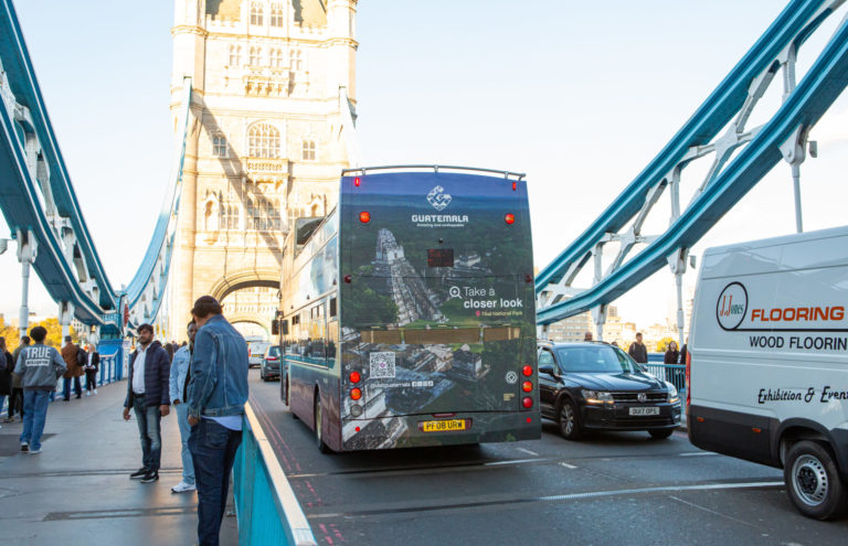Rear view of a double-decker bus on a bridge in London, surrounded by pedestrians and cars.