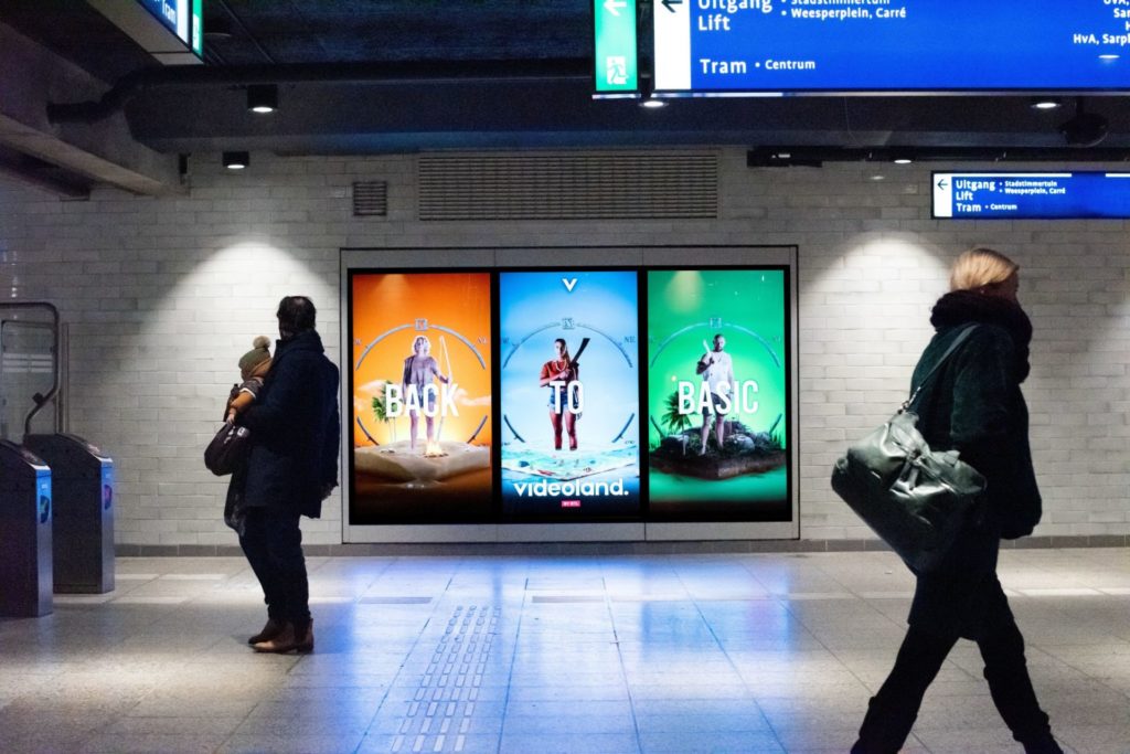 Digital OOH in a train station, people walk past the three screens