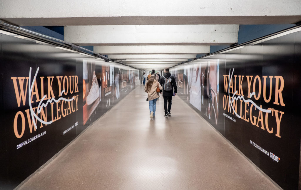 In a pedestrian tunnel that connects subway lines, there are advertisements for Snipes on the left and right walls