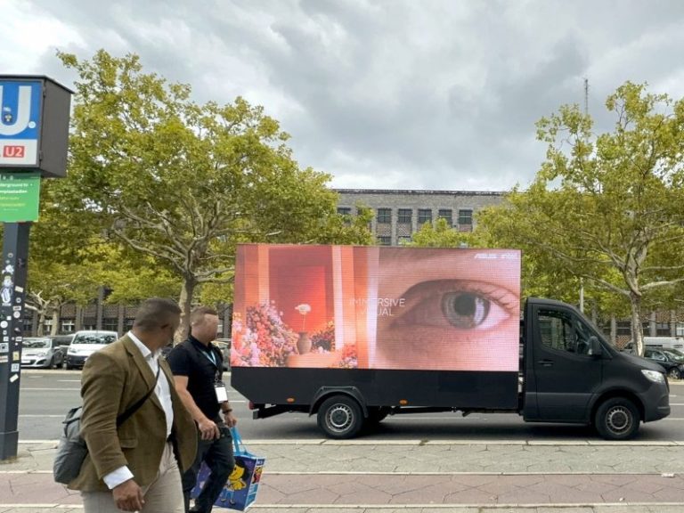 A large digital screen mounted on the left and right of a truck showing an ad for Asus.