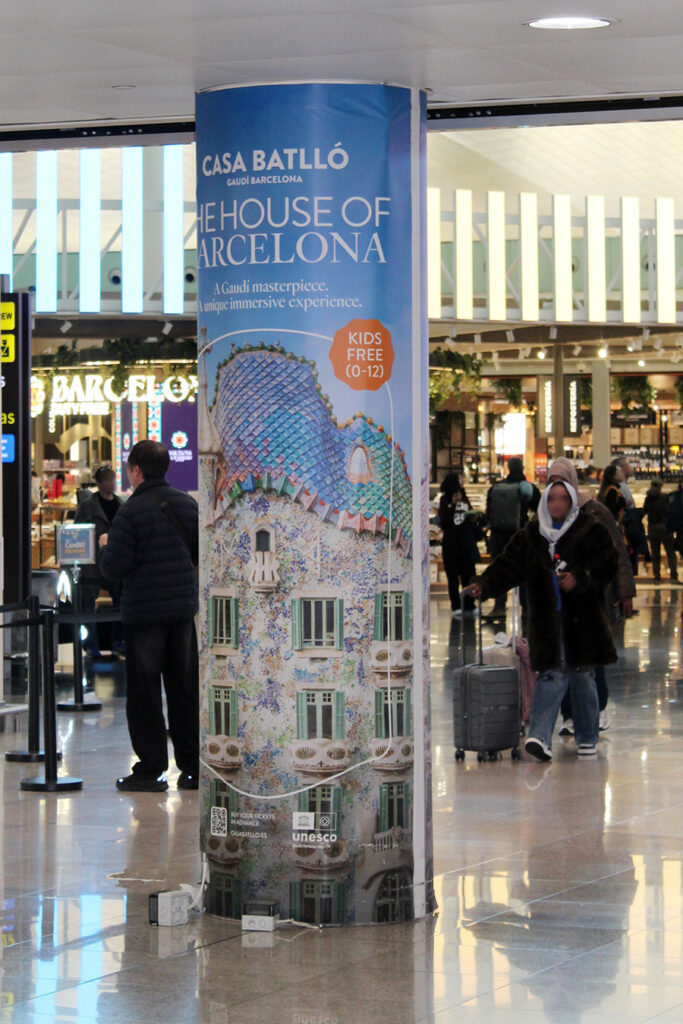 A floor-to-ceiling column at Barcelona Airport, fully wrapped with advertising for the landmark Casa Batlló.