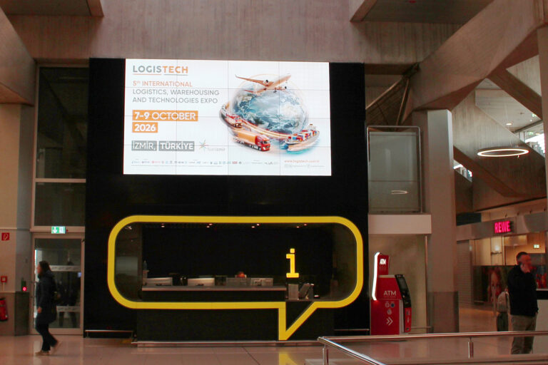 A large, landscape-format digital advertising screen at the airport displays a bright and visually striking advertisement for the Logistech trade fair, which will take place in Izmir in October 2026.