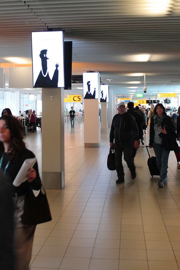 Several portrait format digital City Light Posters on multiple columns at Amsterdam Airport. Two screens are mounted on each column with their backs facing each other. People are walking past the illuminated advertising displays.