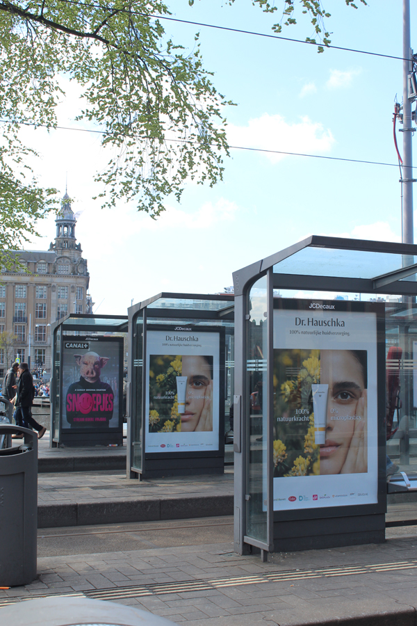 Tram shelters in front of Amsterdam Central Station. Analogue City Light Posters are displayed in the showcases, featuring advertisements for cosmetics and a television series.
