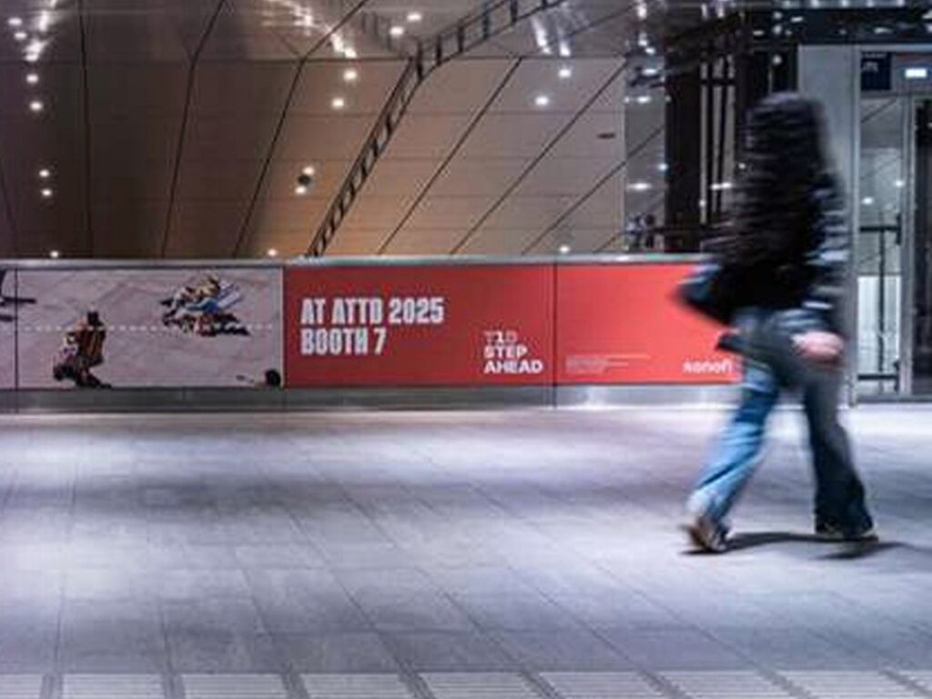 The railing on the intermediate level of the Europaplein subway station. The glass panels are covered with outdoor advertising. A company is promoting its trade show booth.