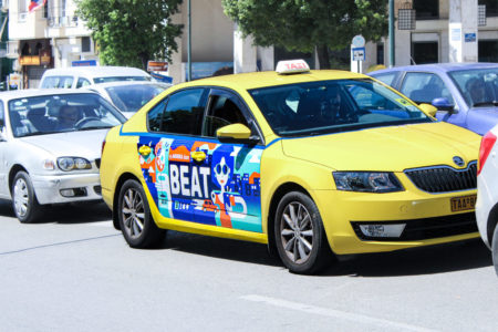 On a street in Athens, a taxi with advertising on the side door (Door-Cover) stands between two cars.