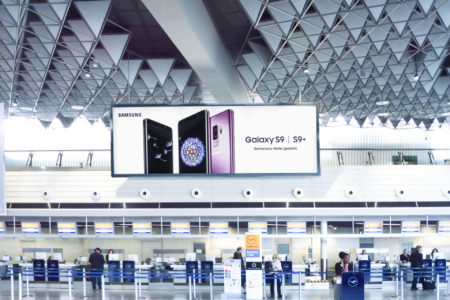 A large digital billboard at the airport in Barcelona displays advertising for a Samsung phone.