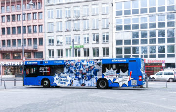 A bus on a street in Cologne has a blue full-cover advertising motif.