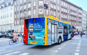 In the city center of Copenhagen, there is a bus with a full-cover motif promoting the car rental app 'Seez.