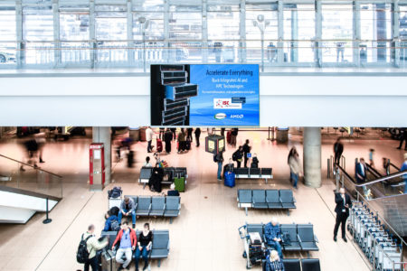 A large digital advertising banner is located in the waiting area at Hamburg Airport.