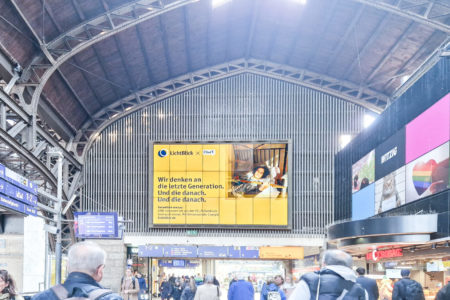 At the train station in Hamburg, a giant poster for 'LichtBlick' is visible, with many people in the foreground