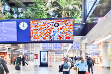 A digital screen at London's airport displays advertising for the 'SBB' transportation company.