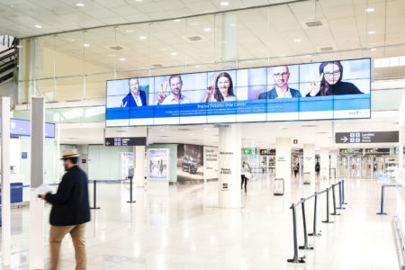 At Madrid Airport, there is a large digital billboard. The digital screen displays people who have conquered cancer.