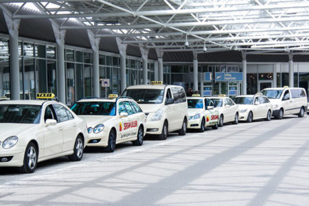 Several taxis with door cover formats are at the departure entrance of Munich Airport, advertising 'Segmüller.