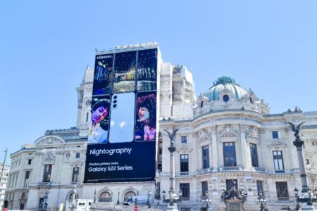 An oversized advertising banner, also known as a Blow Up, has been stretched across a section of a Parisian building facade. The outdoor advertisement for 'Samsung' is displayed in the city center of Paris.