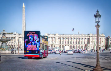 A sightseeing bus touring through Paris, displaying an advertisement for a streaming service called 'Globoplay'.