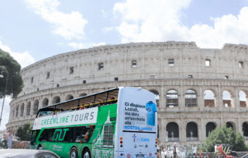 A bus in Rome features advertising for a football association. The Colosseum is visible behind the bus.